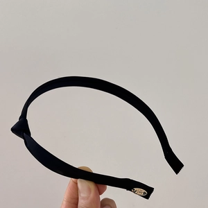 Detail view of black satin knotted headband with gold oval metal logo tag