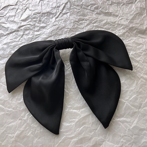 Macro detail of large black satin bow hair clip with soft matte silk texture