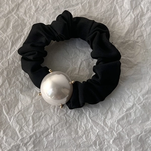 Détail d'une grande perle blanche fixée par des griffes dorées sur un chouchou noir chic