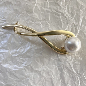 Détail d'une pince à cheveux torsadée dorée ornée d'une grande perle blanche chic