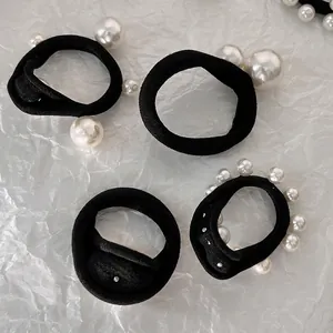 Elastic black hair ties set with hand-stitched faux pearls on white textured background