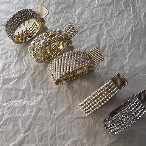 Detailed view of luxury gold hair claws with pearls and rhinestones on a textured background