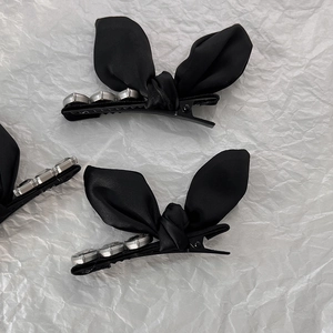 Detailed close-up of a black satin bow hair clip with silver rhinestone edge and duckbill clip