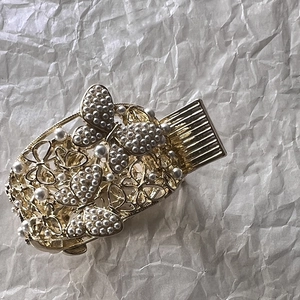 Gros plan d'une pince à cheveux papillon dorée ornée de perles blanches