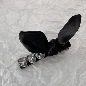 Close-up of black satin bow hair clip featuring three heart-shaped grey crystals