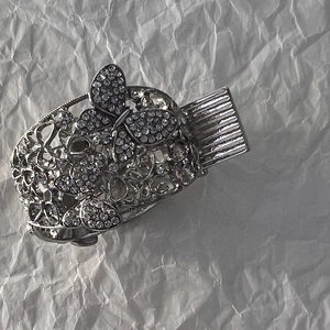 Détail de la pince à cheveux papillon argentée avec strass scintillants sur fond gris