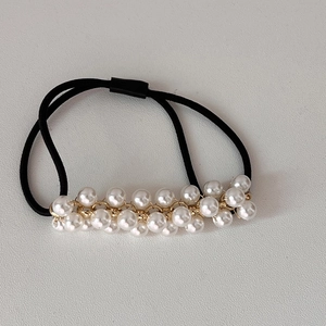 Close-up of black elastic hair tie with double-row white pearls and gold metal links