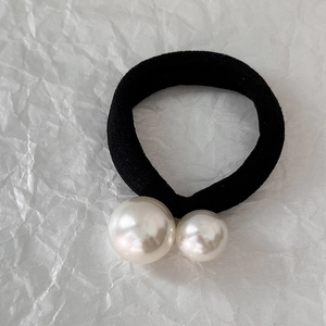 Close-up of black elastic hair tie with dual white pearls on textured background