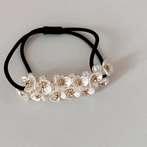 Detail of black elastic hair tie featuring white pearl-like flower charms with gold centers