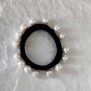 Detail of high-elastic black hair tie featuring smooth white pearls on crinkled paper