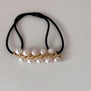 Close-up of black elastic hair tie with white imitation pearls and gold chain links