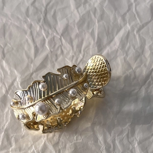Vue macro d'une pince à cheveux feuille dorée ornée d'élégantes perles blanches