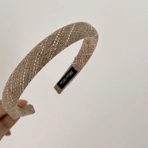Close-up of brown textured sponge headband with white diagonal stitching and handmade label