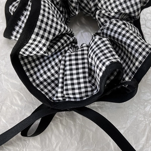 Close-up of black and white gingham scrunchie with long satin ribbons on white paper