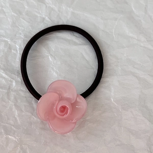 Dettaglio di un fiore di camelia in resina rosa su un elastico per capelli nero flessibile