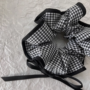 Detail of gingham scrunchie with black trim and long ribbon bow on white paper