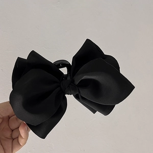 Close-up of a large black satin bow hair claw clip held in hand for hair styling