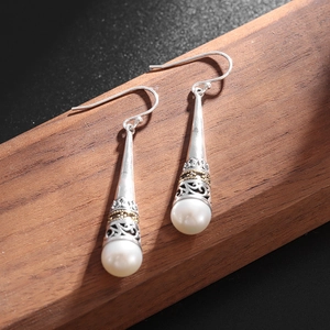 Macro detail of silver-plated vintage crown drop earrings with teardrop pearls on wood