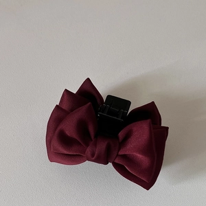Détail d'une pince à cheveux avec nœud en satin rouge vin et griffe en plastique noir