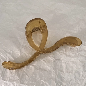 Detail of a large amber jelly shark hair clip with a stylish twisted design on white paper