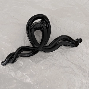 Détail d'une grande pince à cheveux noire nacrée en forme de vague sur papier froissé