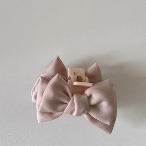 Détail d'une pince à cheveux à nœud en satin rose sur un fond gris épuré et simple