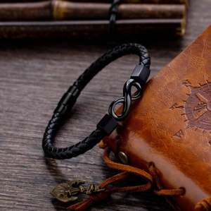 Men's black braided leather infinity bracelet with magnetic clasp on a brown notebook