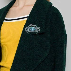 Exaggerated crab shaped brooch with colorful blue rhinestones on a green coat lapel