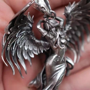 Detailed close-up of a vintage silver angel pendant with intricate wings held in hand