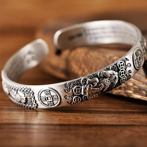 Makroaufnahme eines Vintage-Silberarmbandes mit Pixiu-Relief und glückbringenden Münzen