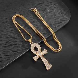 Dettaglio del ciondolo a croce Ankh dorata con strass scintillanti su catena a maglia
