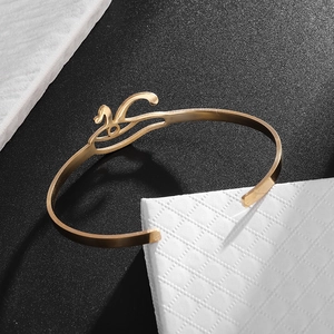 Detail view of gold stainless steel open bangle with elegant swan design on dark surface