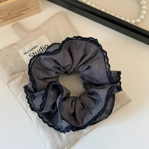 Detailed close-up of dark grey scrunchie with black lace edges on a linen cushion