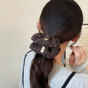 Detailed view of coffee velvet polka dot scrunchie with a gold heart charm and handmade tag