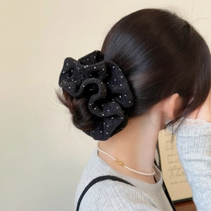 Detail of a large black polka dot velvet scrunchie worn on a low bun in French style