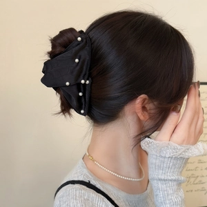 Macro shot of a black satin bow hair claw with pearl accents on a French bun hairstyle