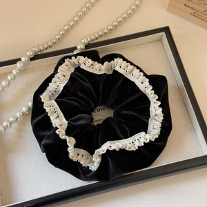 Detail of a velvet scrunchie with white lace trim displayed with elegant pearls