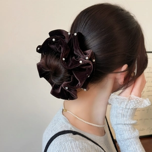 Detail of a dark brown velvet hair scrunchie with white pearls on a model bun