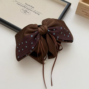 Detail of a brown satin bow hair clip with polka dots and long pearl-tipped ribbons