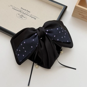 Close-up of black satin bow hair clip with polka dots and dangling pearl charms