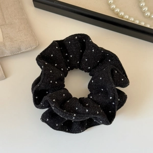 Close-up of black velvet scrunchie with white polka dots on a minimalist background