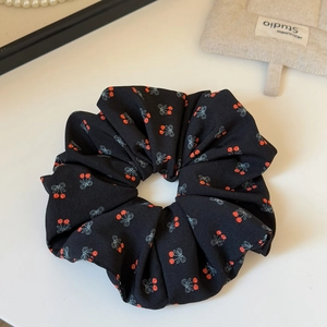Dettaglio di scrunchie nero con motivi di ciliegie rosse e fiocchi blu eleganti