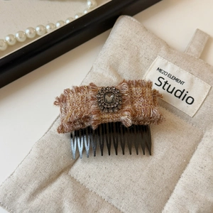 Dettaglio della molletta a fiocco in tweed con diamante grigio su sfondo in tessuto beige