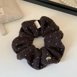 Detail of a brown velvet polka dot scrunchie with a handmade tag and golden bow charm