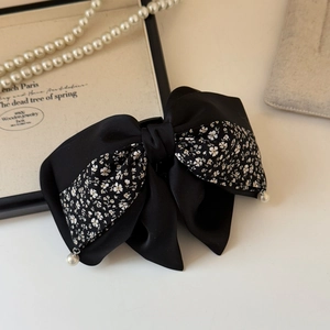 Detail of elegant black satin bow hair clip with floral pattern and pearl pendants