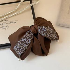 Detailed shot of brown satin bow hair clip with floral patterns and pearl drops