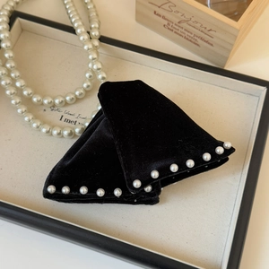 Close-up of black velvet triangle hair claws with pearl trim on a display tray