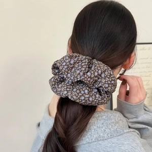 Detailed view of a dark brown floral scrunchie on a ponytail with soft blue flower patterns