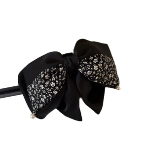 Elegant black bow hair clip with white floral patterns and hanging pearl accents