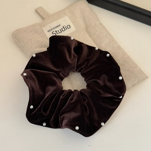Close-up of brown velvet scrunchie with white pearl detailing on a beige background